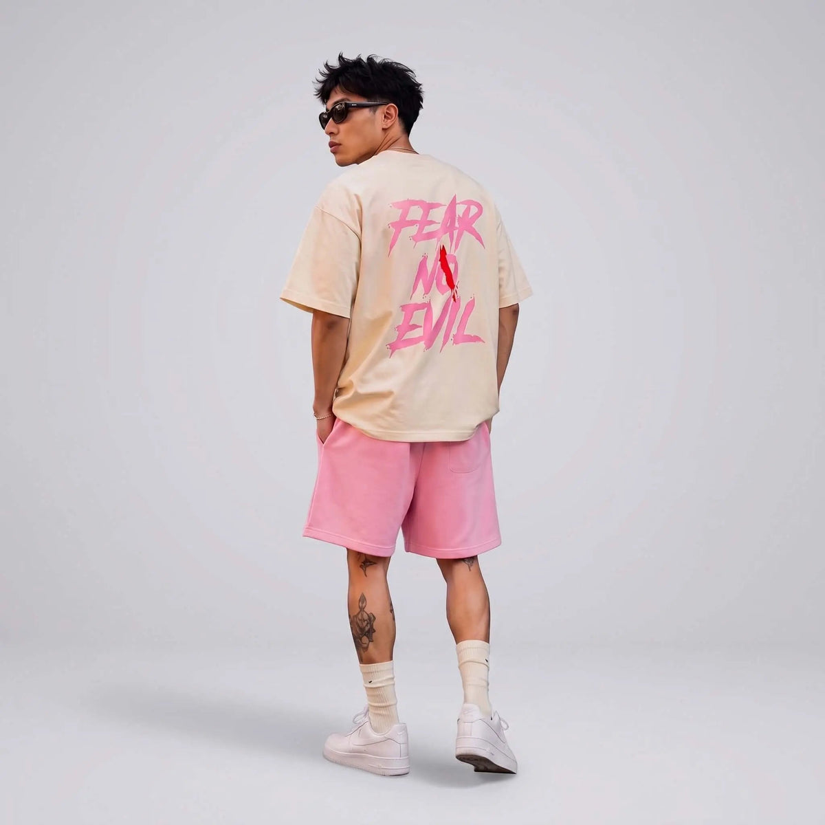A model in faith-inspired streetwear clothing featuring a pastel shirt and pink shorts with bold text.
