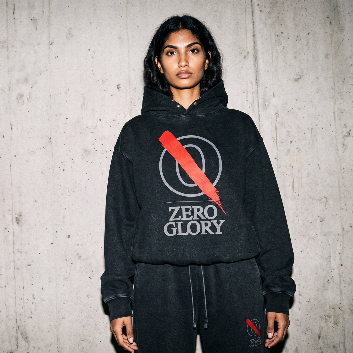 Model wearing the black Overcast heavyweight unisex hoodie with a red lightning bolt graphic and white text, paired with black sweatpants, against a textured concrete wall