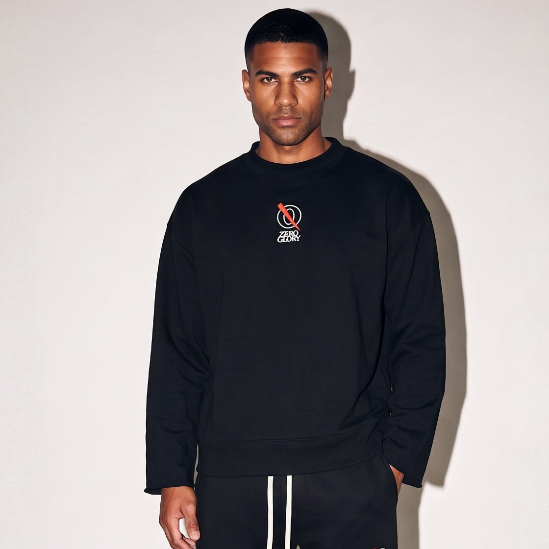 A man modeling a black crewneck sweatshirt and matching black sweatpants with white drawstrings, standing against a white studio backdrop.