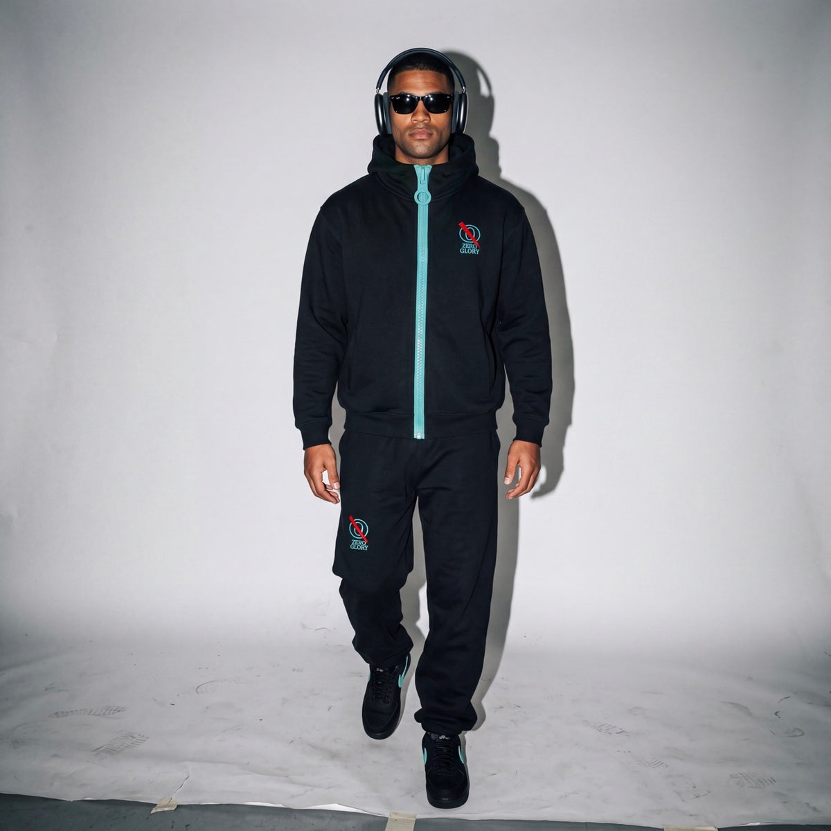 Man wearing the Zero Glory Unisex Oversized Fleece Chunky-Zip Hoodie in Black with the blue chunky zipper and Barrel Leg Sweatpants