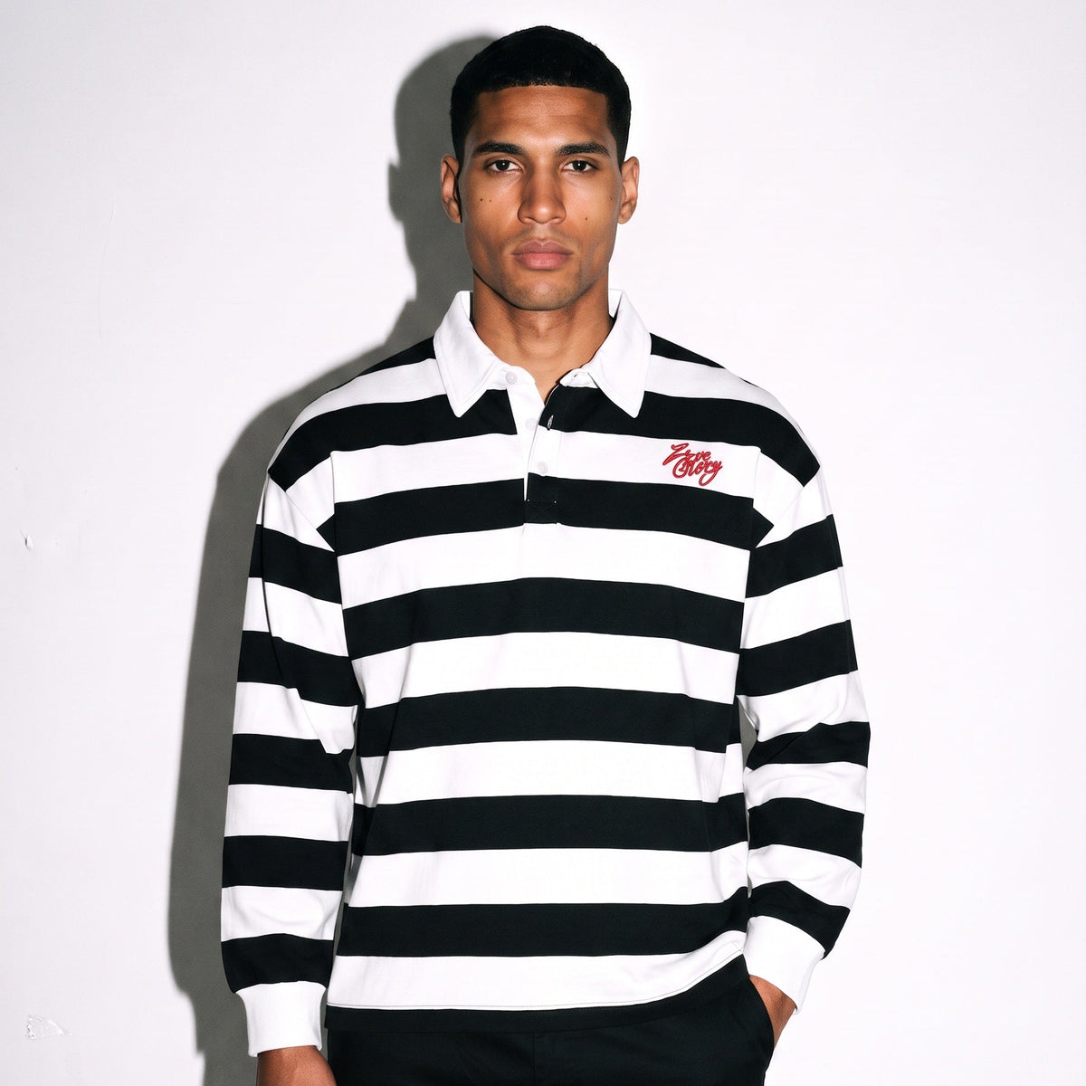 Model wearing striped long sleeve polo with black and white stripes and logo, showcasing relaxed streetwear style.