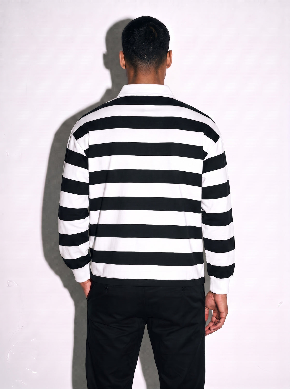 Back view of a man wearing a striped long sleeve polo with black and white stripes.