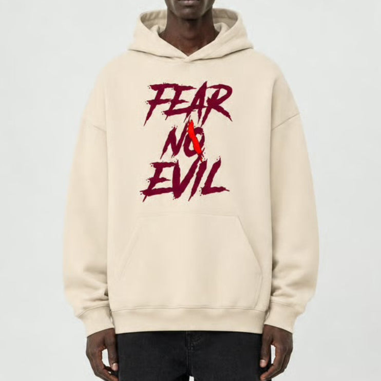 A model stands against a light gray studio background wearing a cream-colored hoodie with a red and black 'FEAR NO EVIL' graphic on the chest, paired with black wide-leg pants and black shoes.