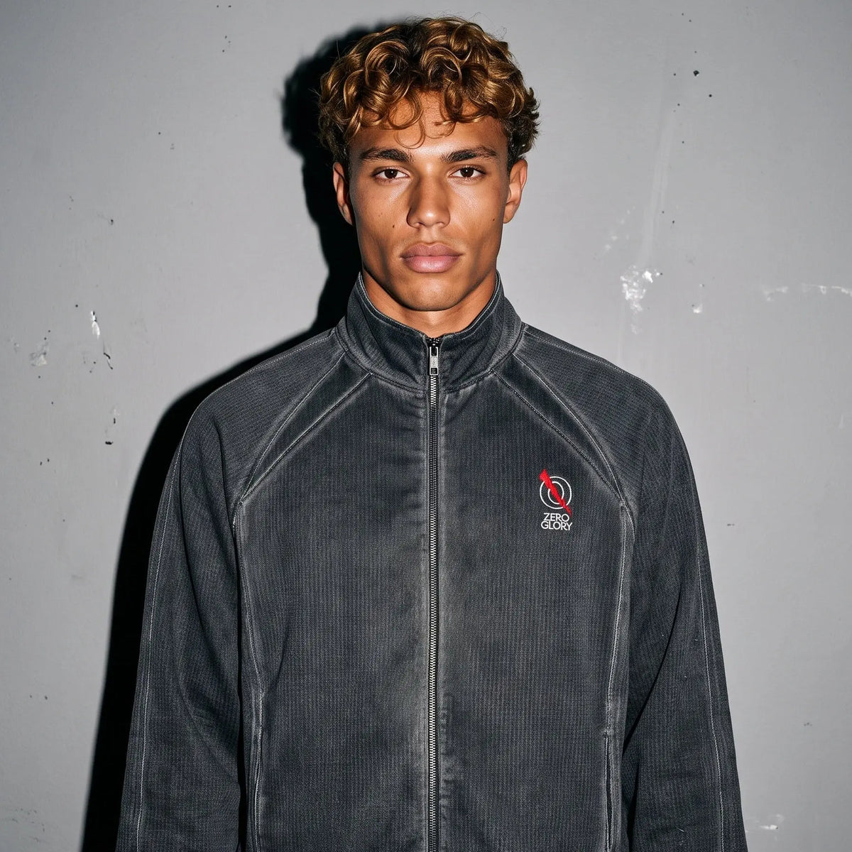 Model wearing a charcoal wash unisex track jacket, featuring a full-zip closure and stand collar, against a plain background.