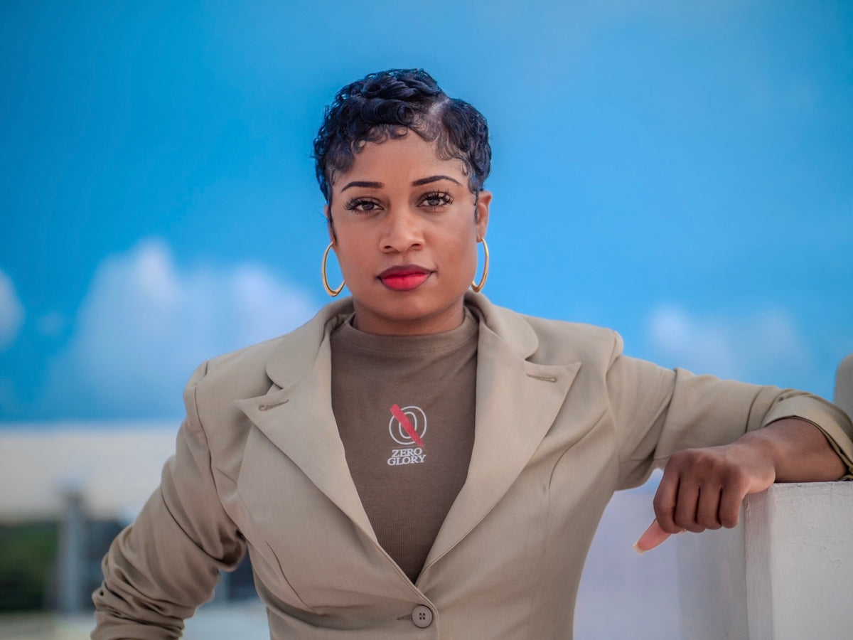 Zero Glory founder wearing a taupe blazer and branded brown top featuring the Zero Glory logo.