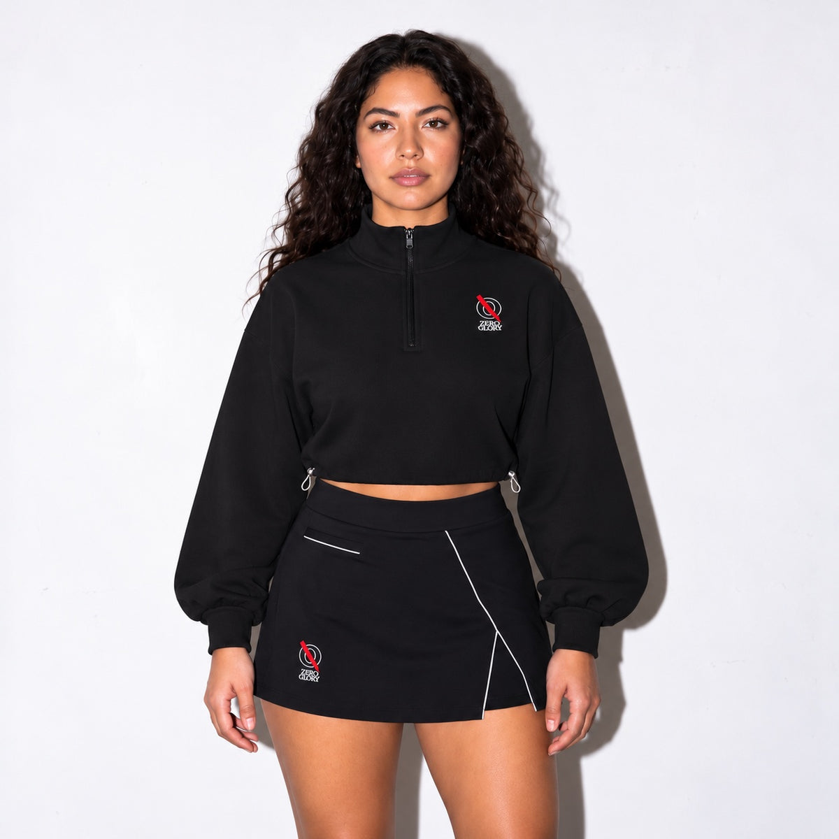 Zero Glory Women's Mock-Neck Quarter-Zip Sweatshirt in black worn with the Women's High-Waist Performance Skort