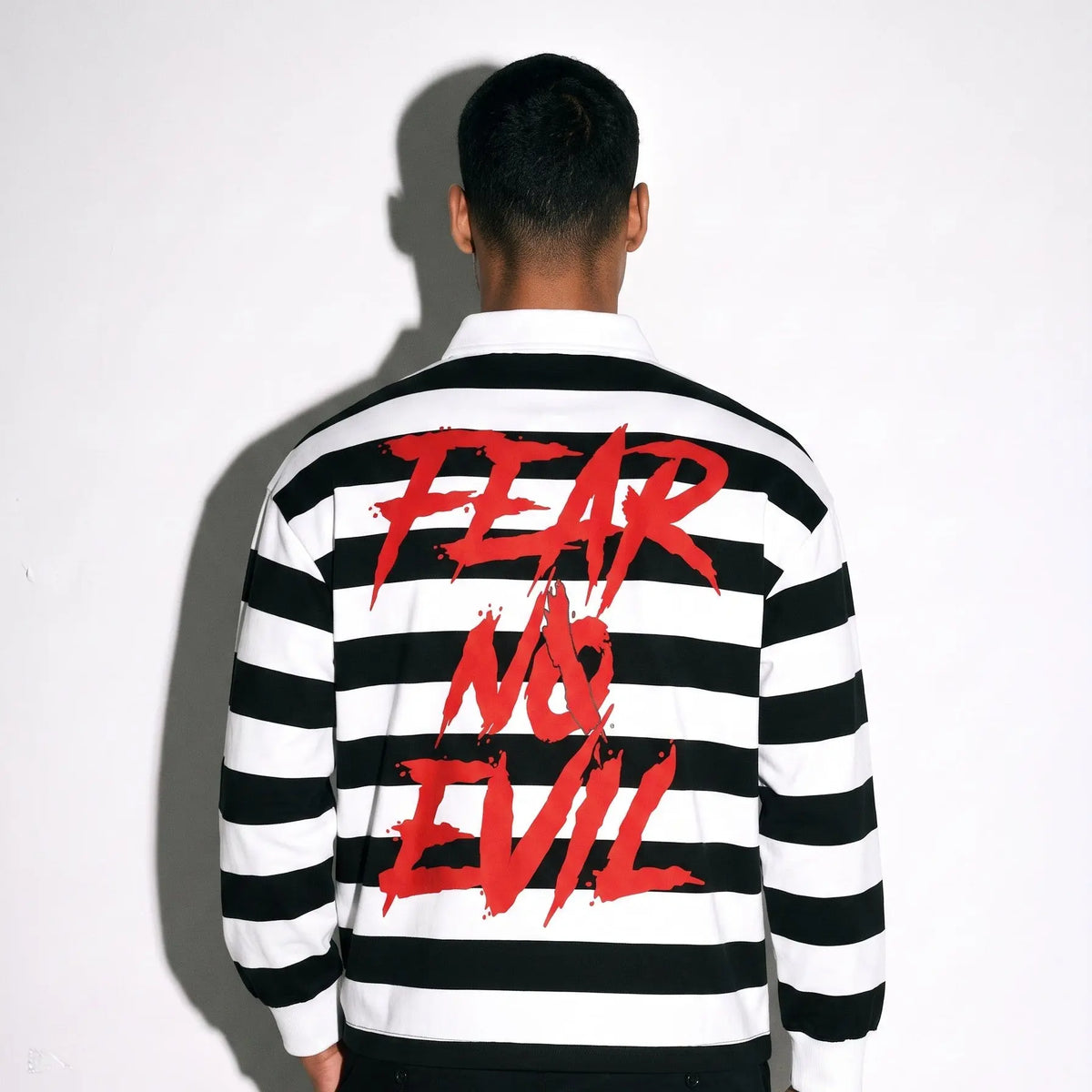 Back view of a man wearing a striped long sleeve polo with bold 'FEAR NO EVIL' text in red on a black and white background.